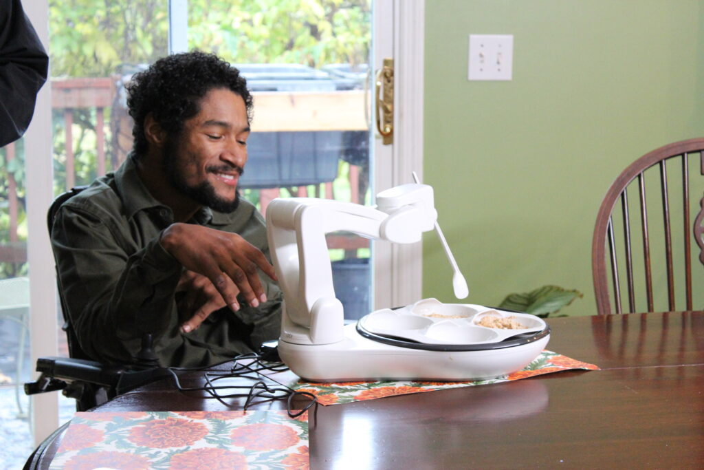 Marcos uses obi feeder while seated at a table.
